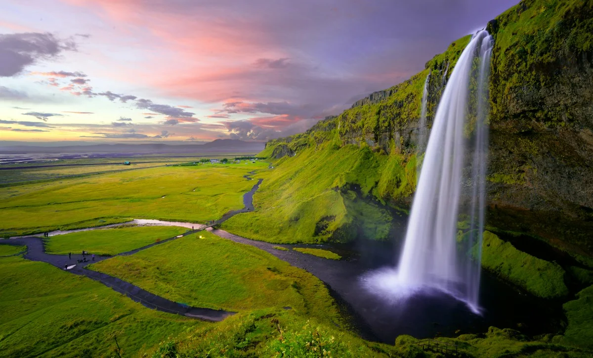 Waterfall dropping beside green cliffs and an open valley