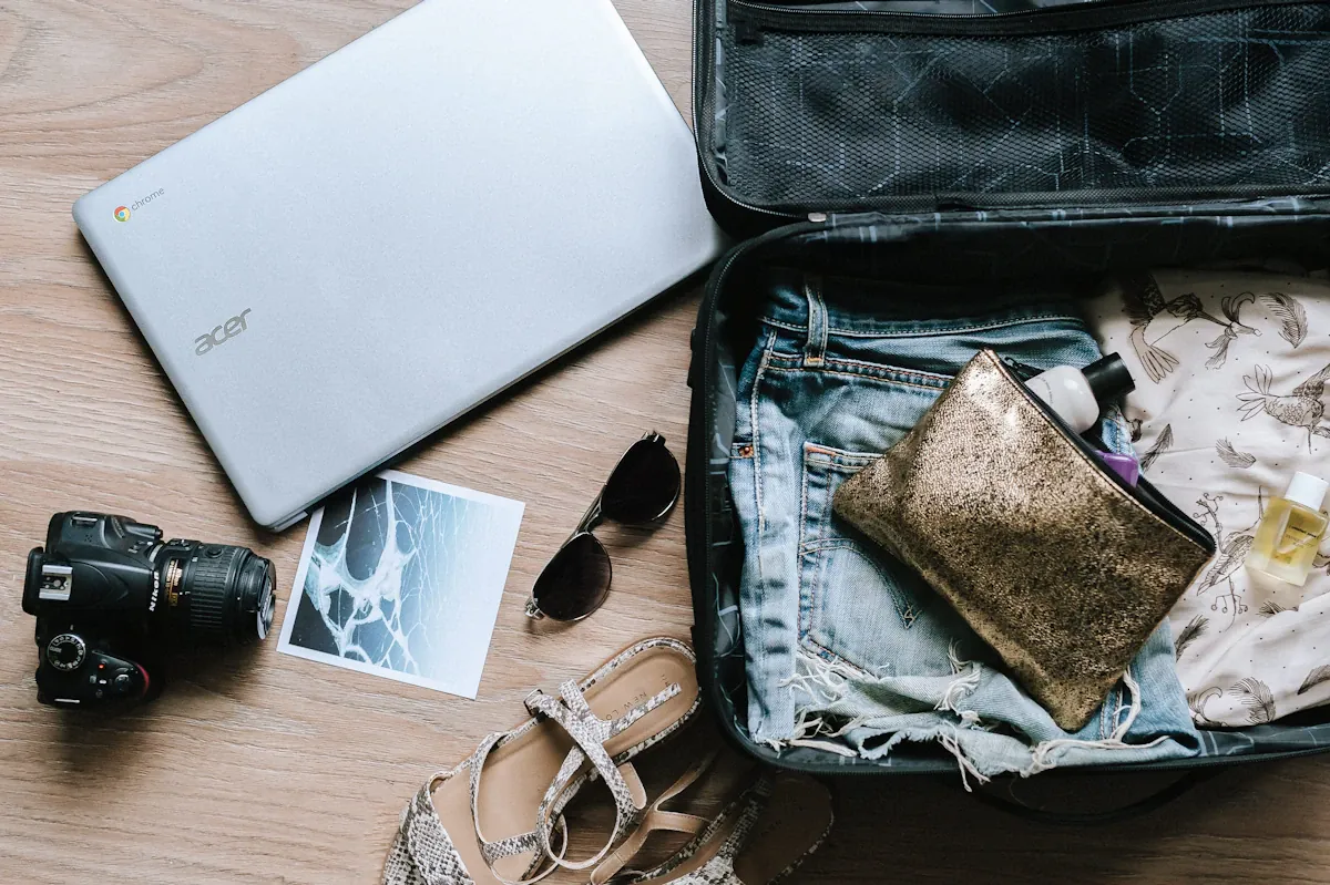An open suitcase with clothing, a pouch, camera and nearby travel belongings