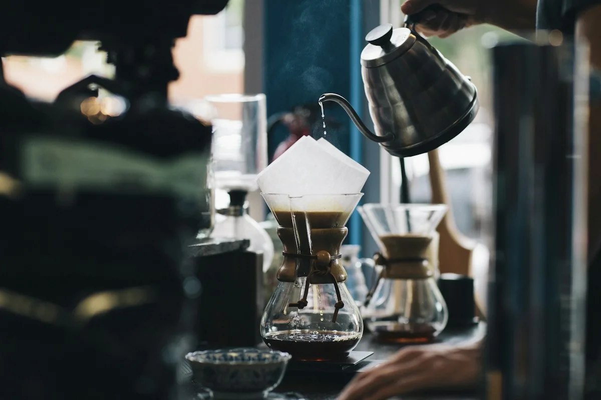 A black kettle pouring water into coffee brewing equipment
