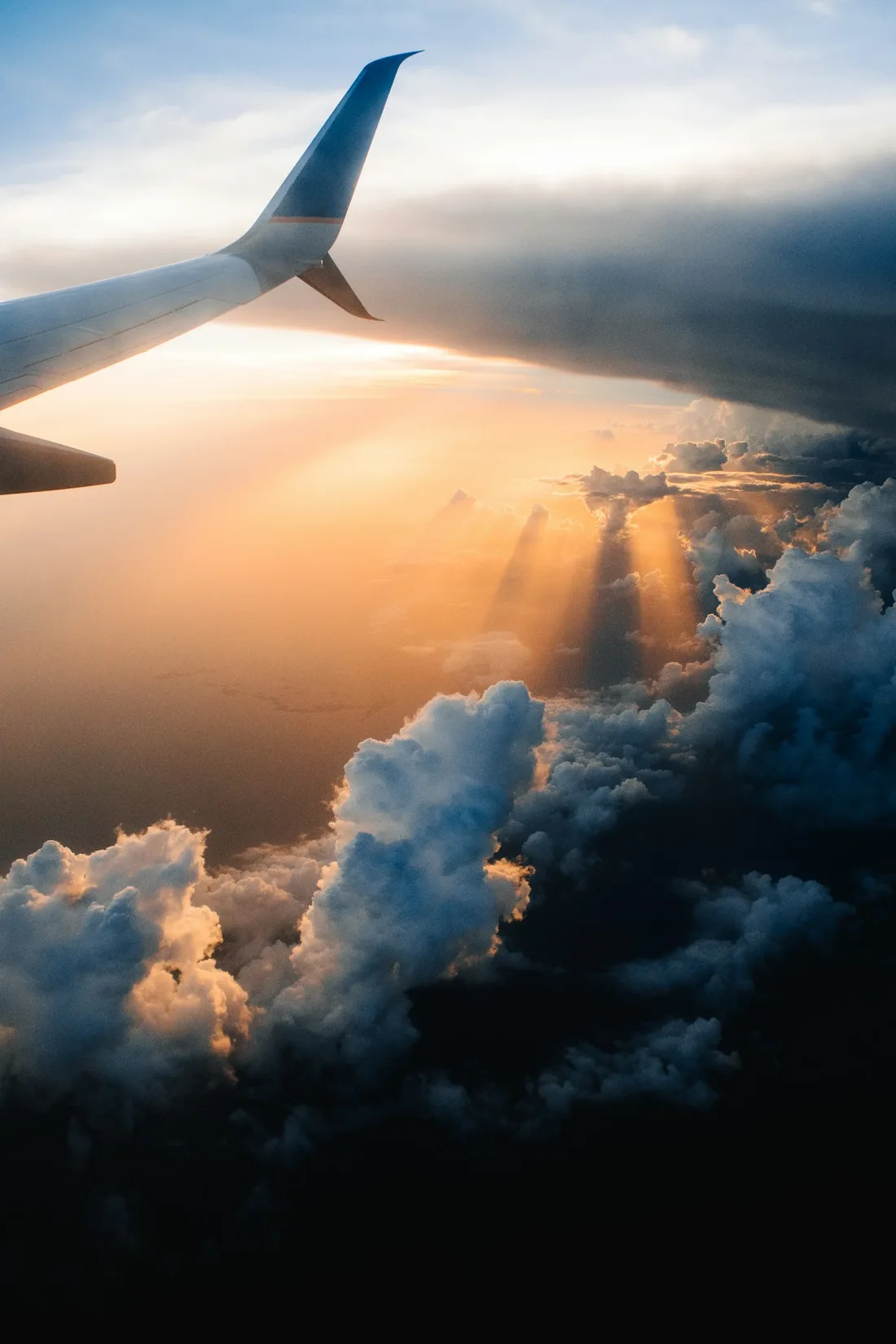 Airplane wing beside sunlit clouds and a warm sky