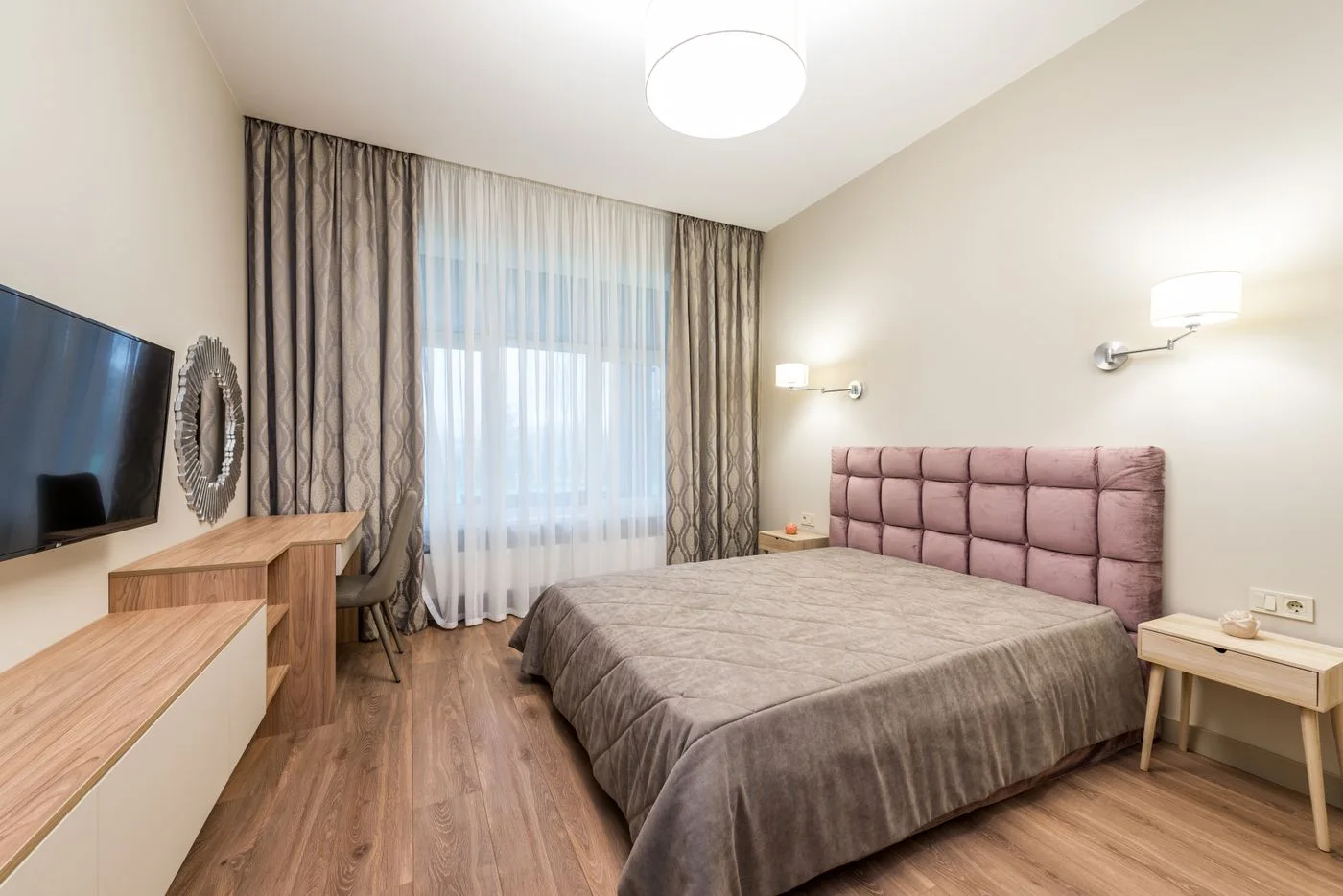 A bedroom with television, curtains and a padded headboard
