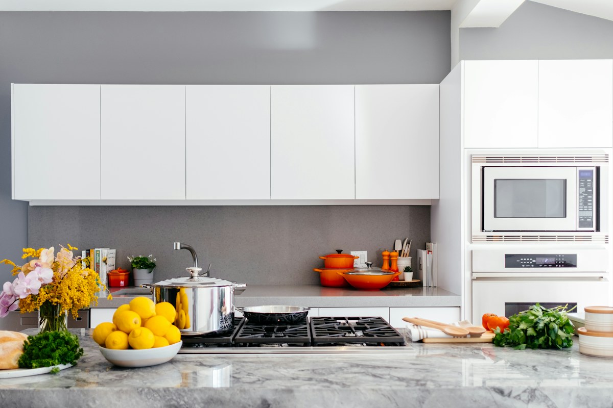 A pale kitchen with a hob, pots, fruit and integrated appliances