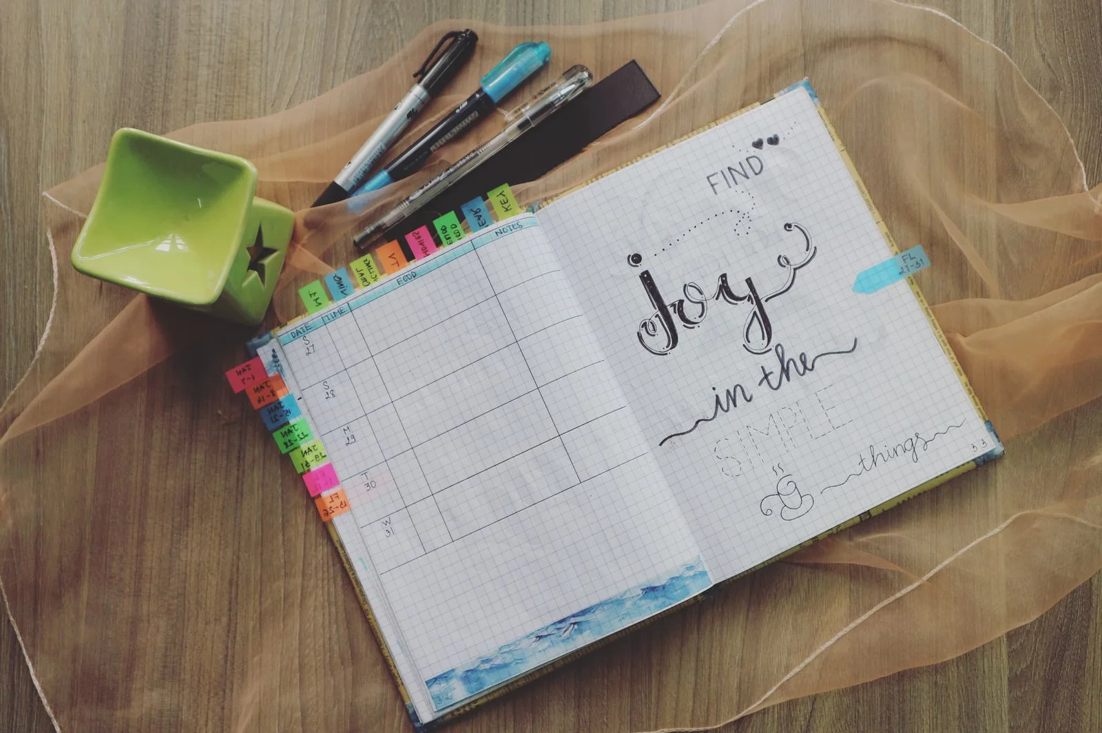 An open planner with pens, coloured tabs and a small green dish