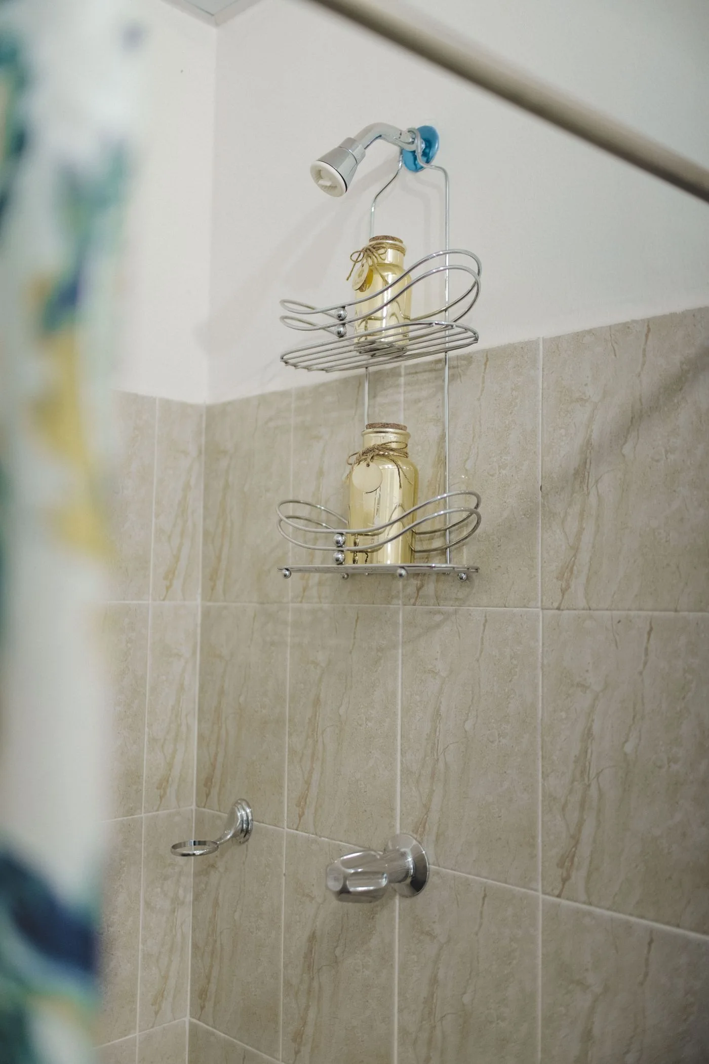 A wire shower shelf holding a bottle against pale tiles