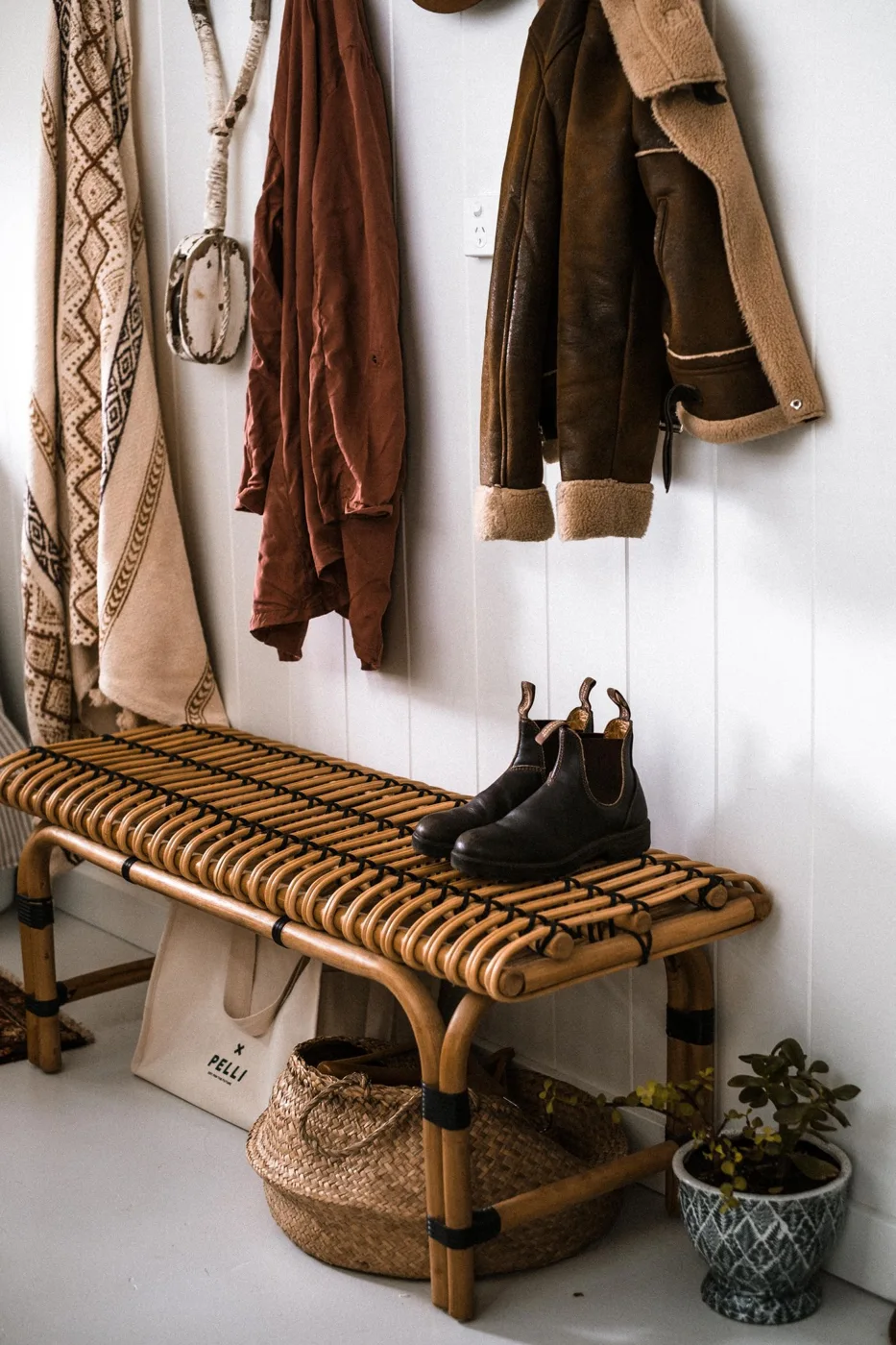 Coats and boots arranged around a woven hallway bench
