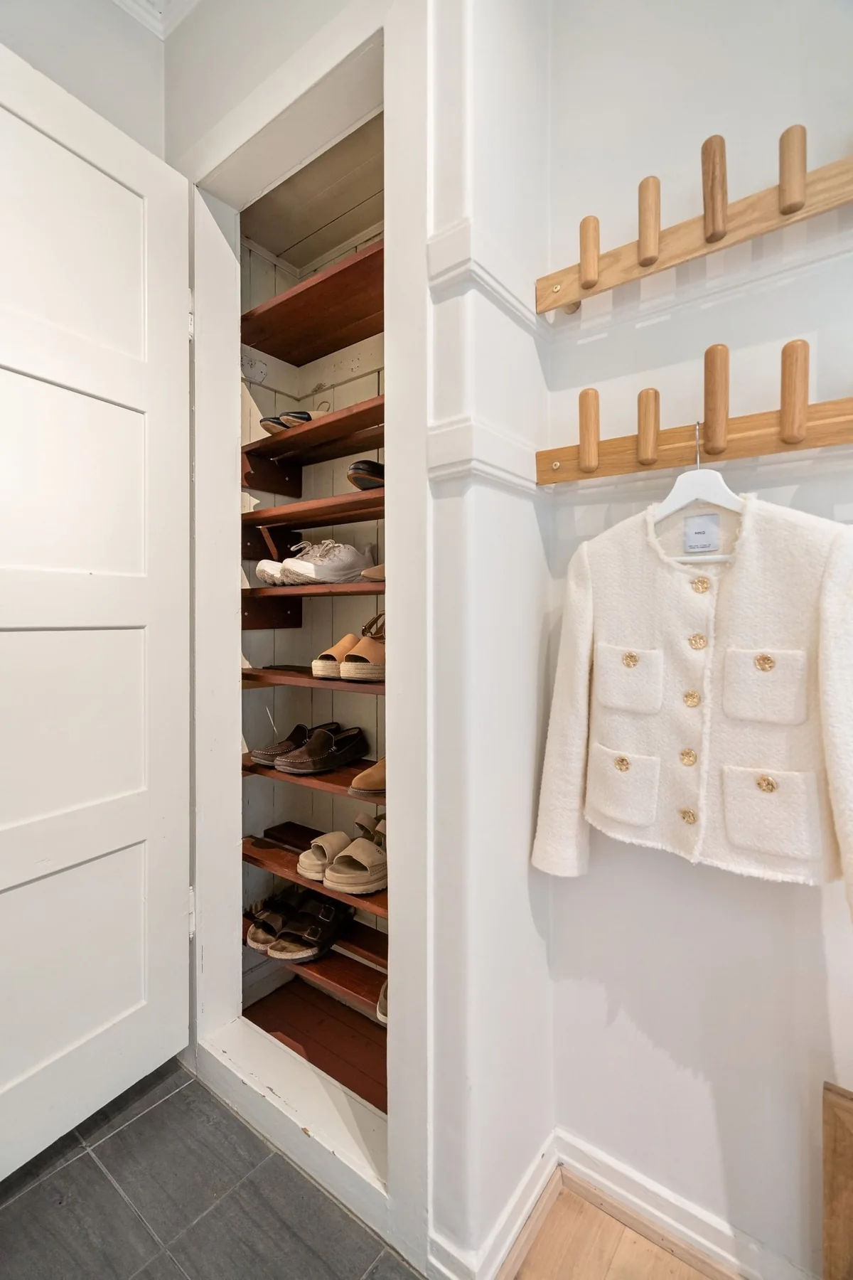 An open wardrobe with shelves beside a pale jacket hanging on wall hooks