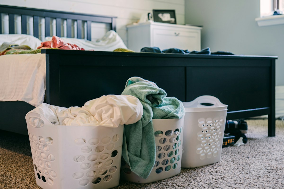 Laundry baskets with clothes beside a bed