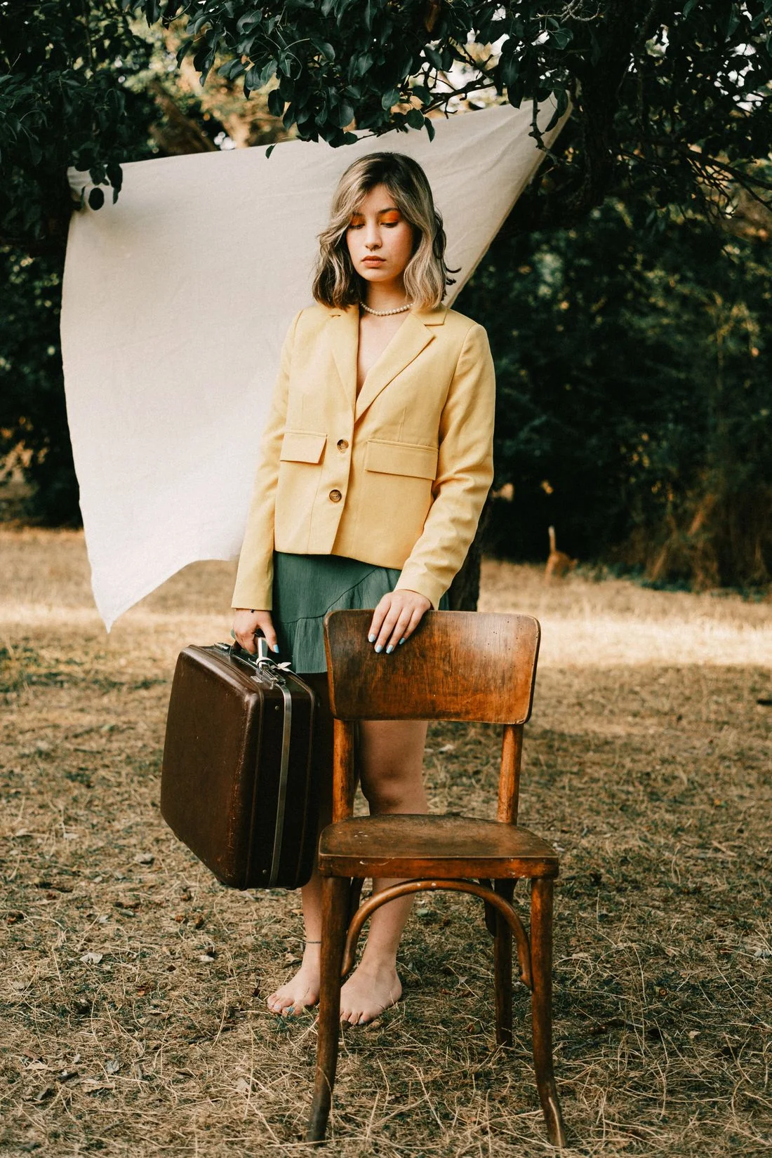 Woman wearing a yellow blazer and holding a suitcase outdoors