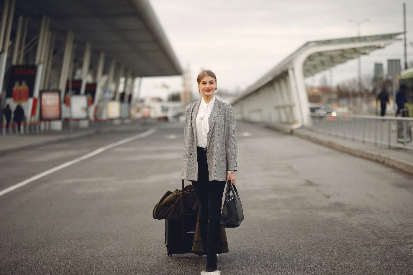 Woman in a gray jacket carrying bags outside a terminal